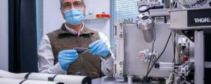 Ángel Pérez stands with a sample of a hybrid electrode in front of a laser installed in a lab.