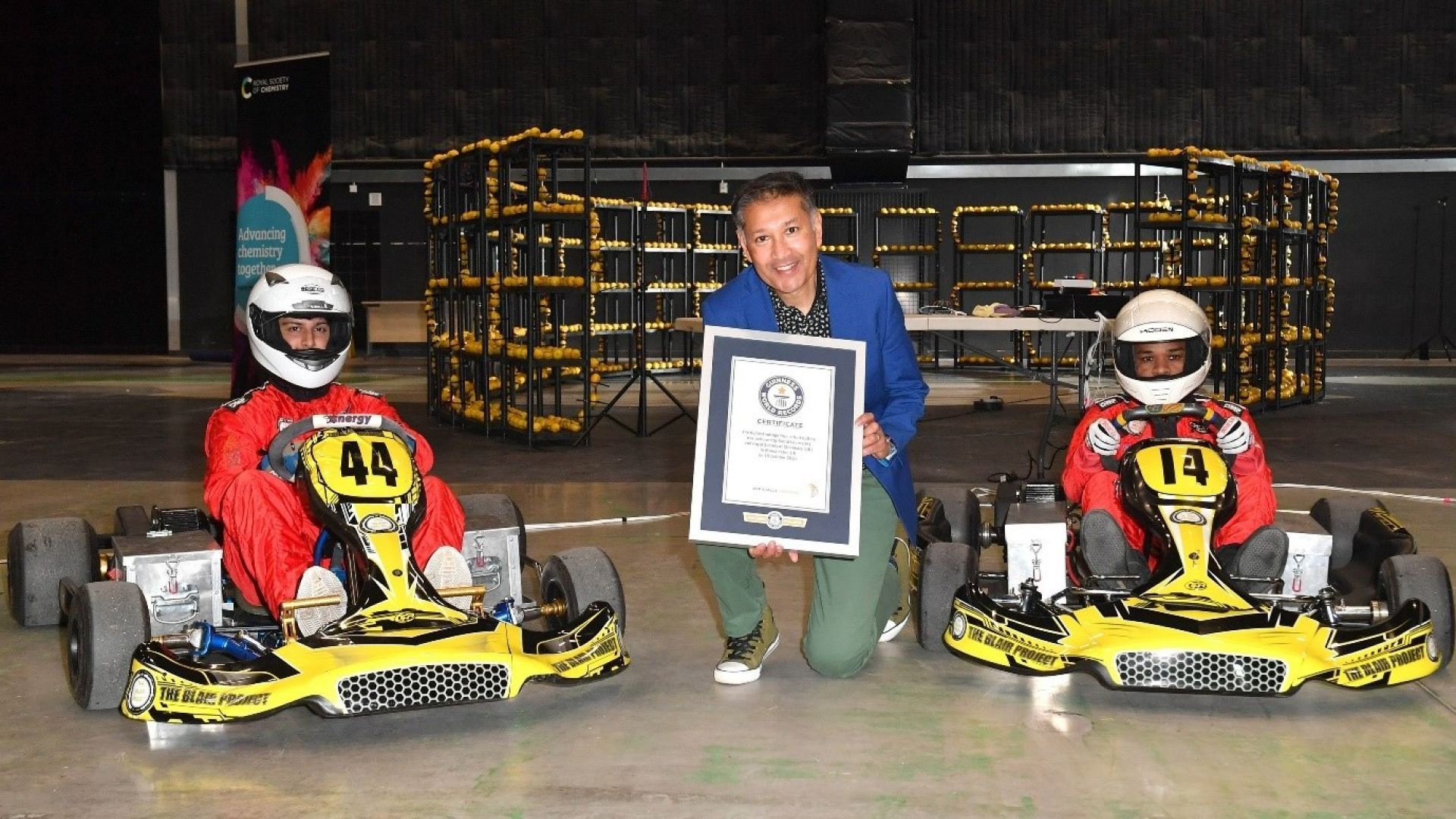 Professor Saiful Islam holding the official GUINNESS WORLD RECORDS™ certificate alongside two go-karts used in the race
